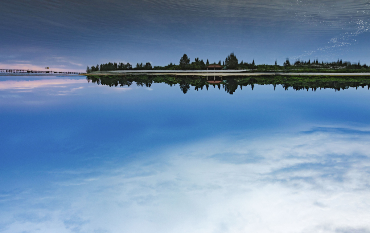 從西表島眺望由布島的景色。在黎明前的短暫瞬間，藍天倒映在水面上，形成如鏡子般美麗的畫面